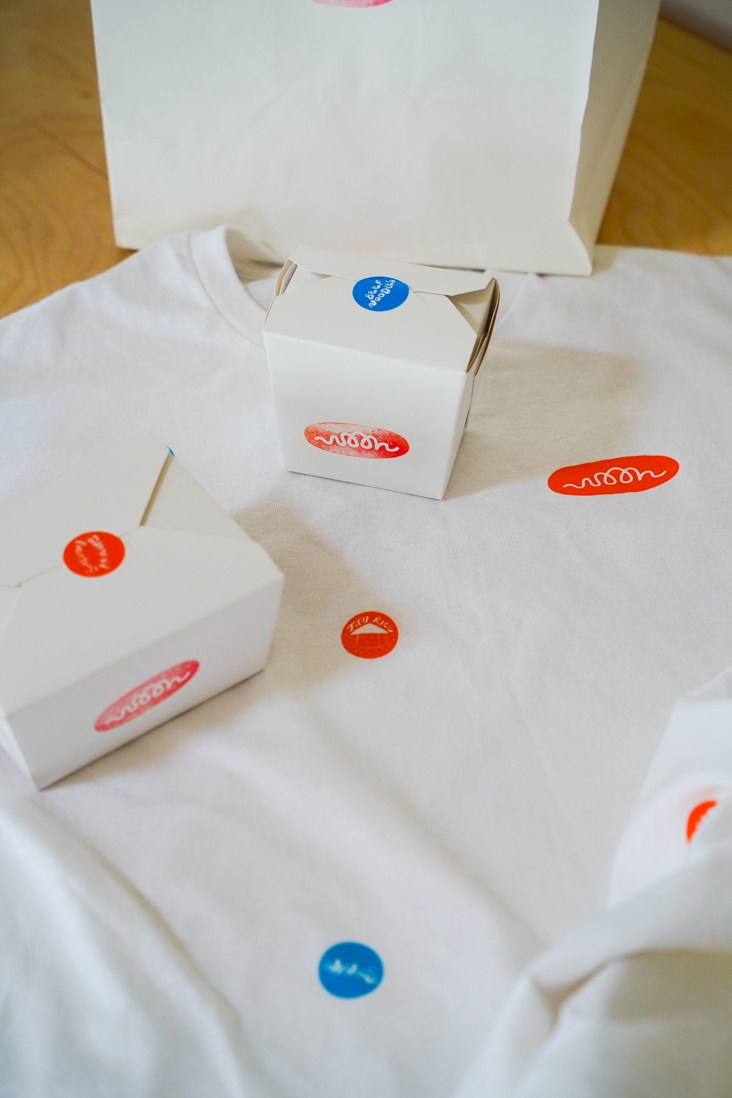 A white tee shirt with take out stickers printed on it and take out boxes around it