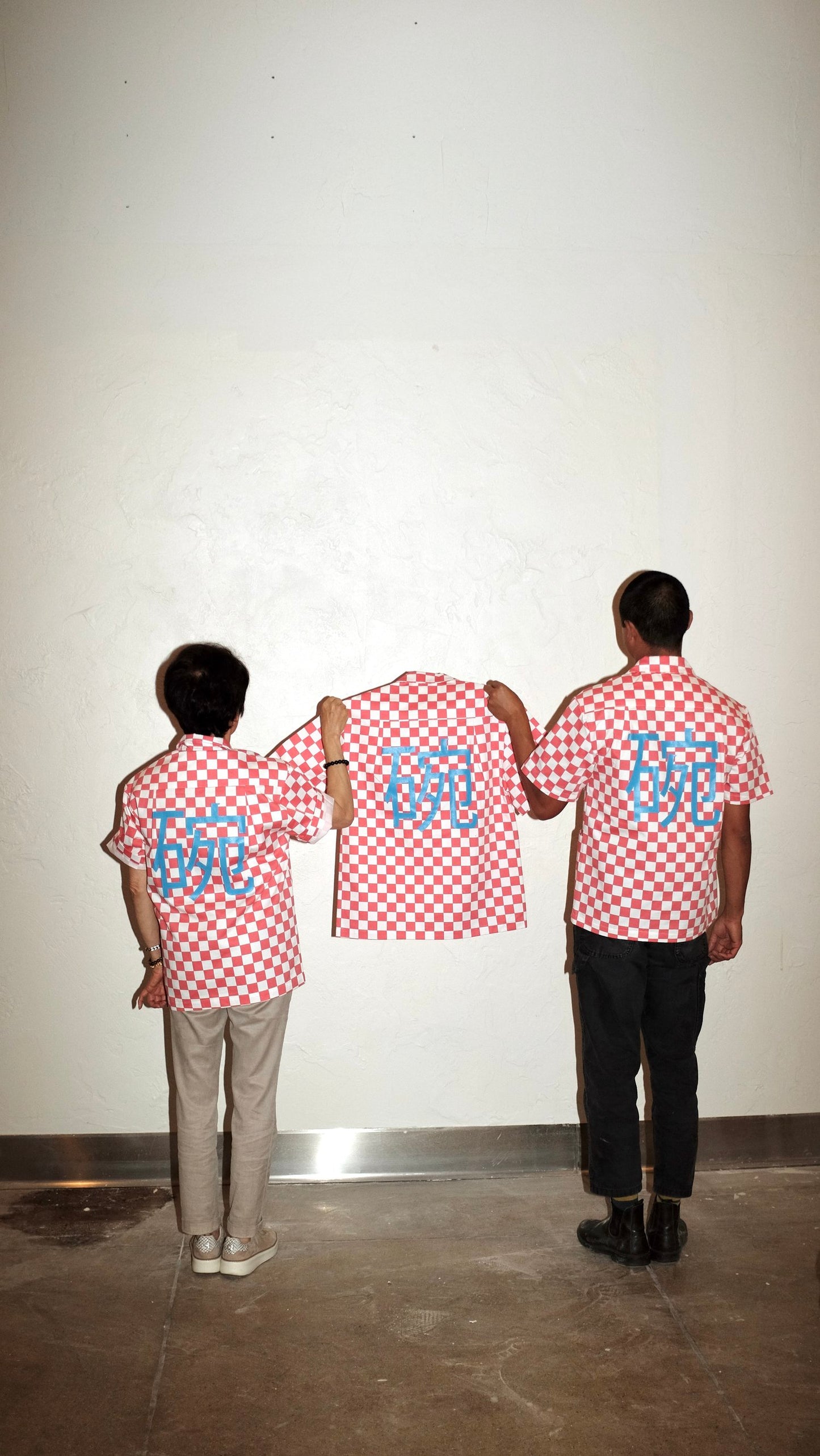 Two people wearing red checkered work shirts holding another red checkered work shirt showing the back