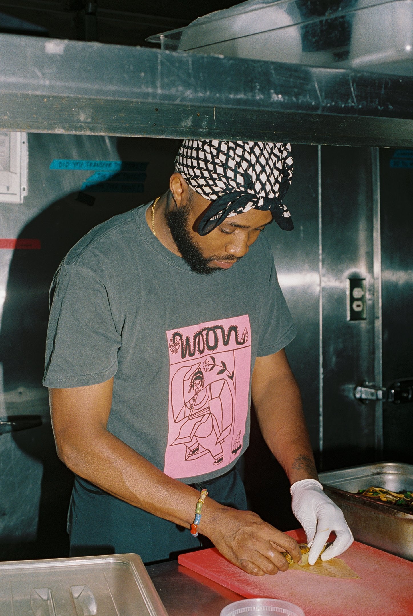 Person wearing a gray tee shirt with pink picture on it, working in a kitchen.