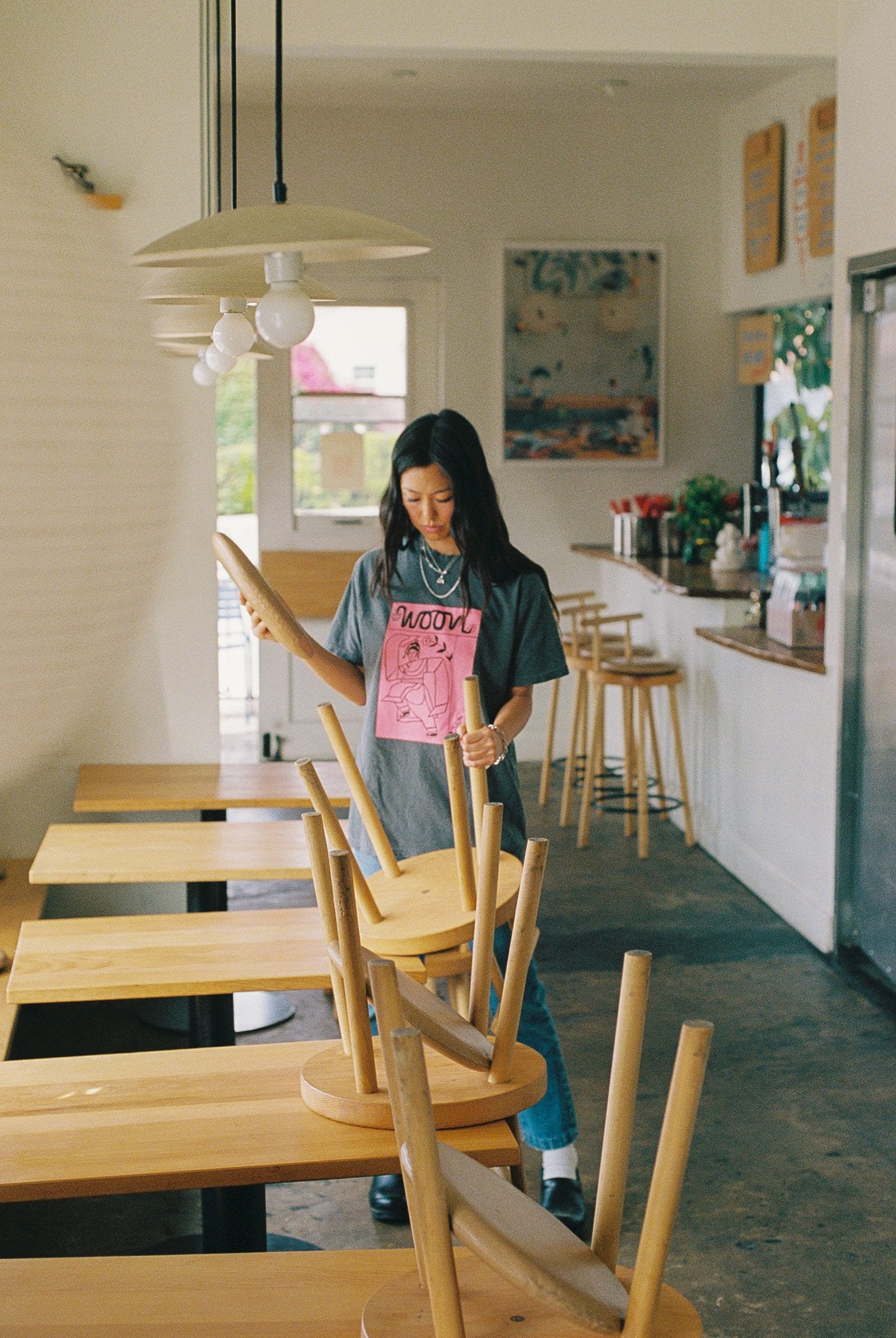 Person wearing a gray tee shirt with pink picture on it. Standing in a restaurant.