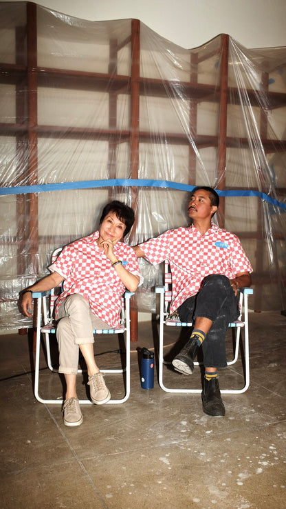 Two people wearing red checkered work shirts sitting on chairs