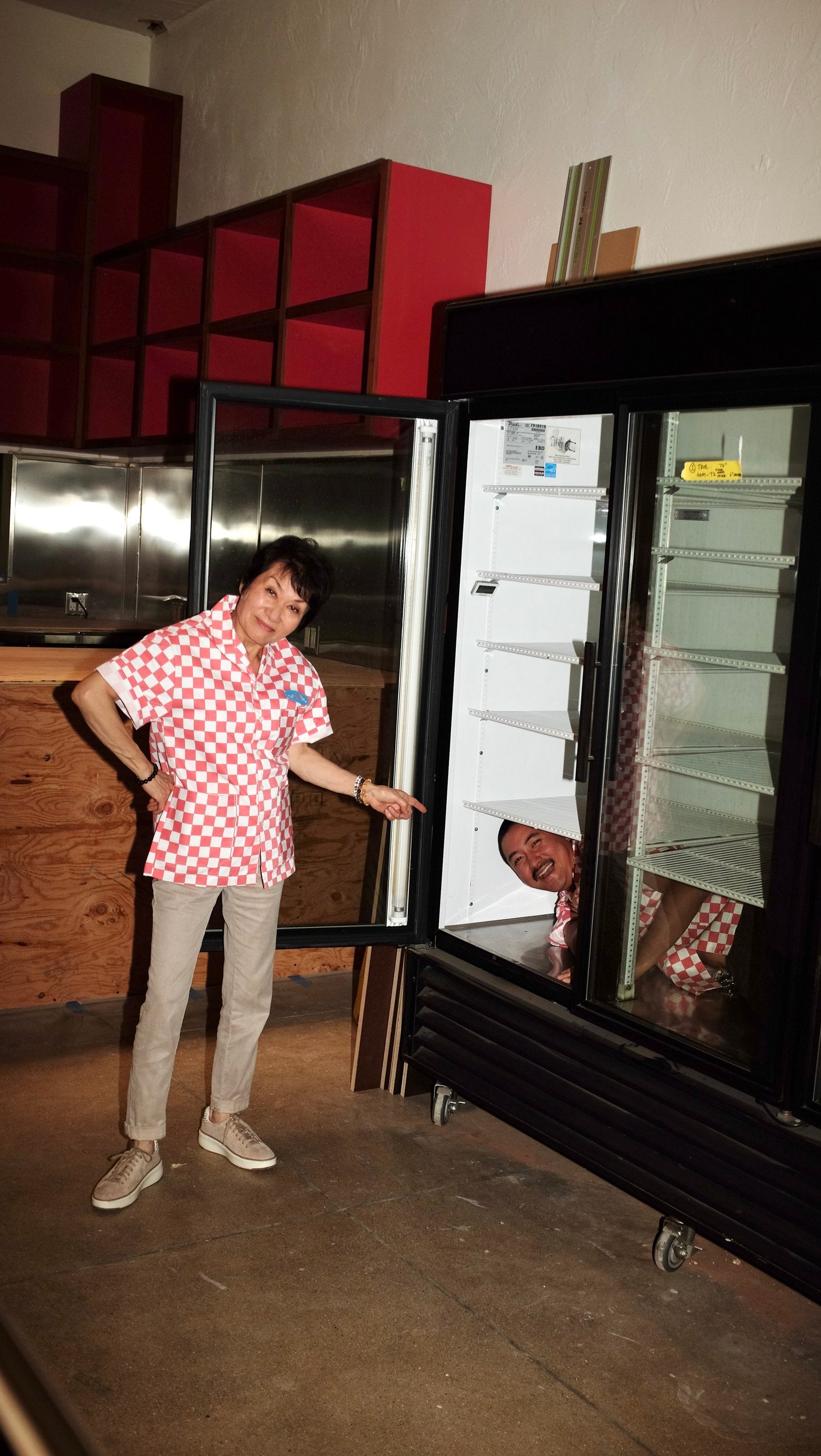A person inside of a cooler and another person pointing. Both people wearing red checkered work shirts