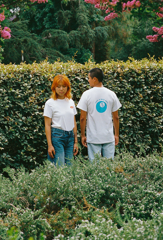 Two people standing in bushes with white tee shirts on