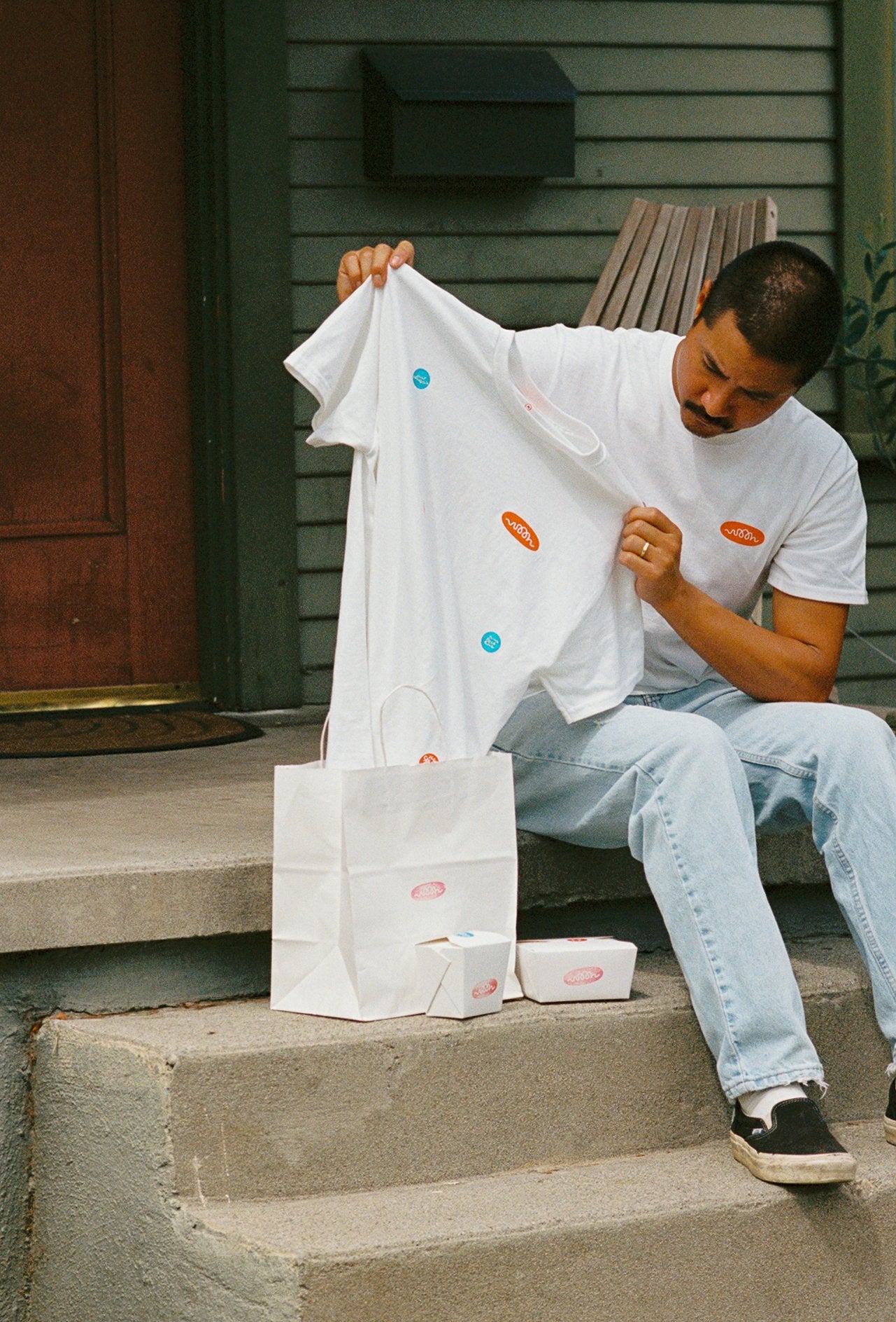 A person pulling a white t shirt out of bag. The tee shirt has take out stickers printed all over it